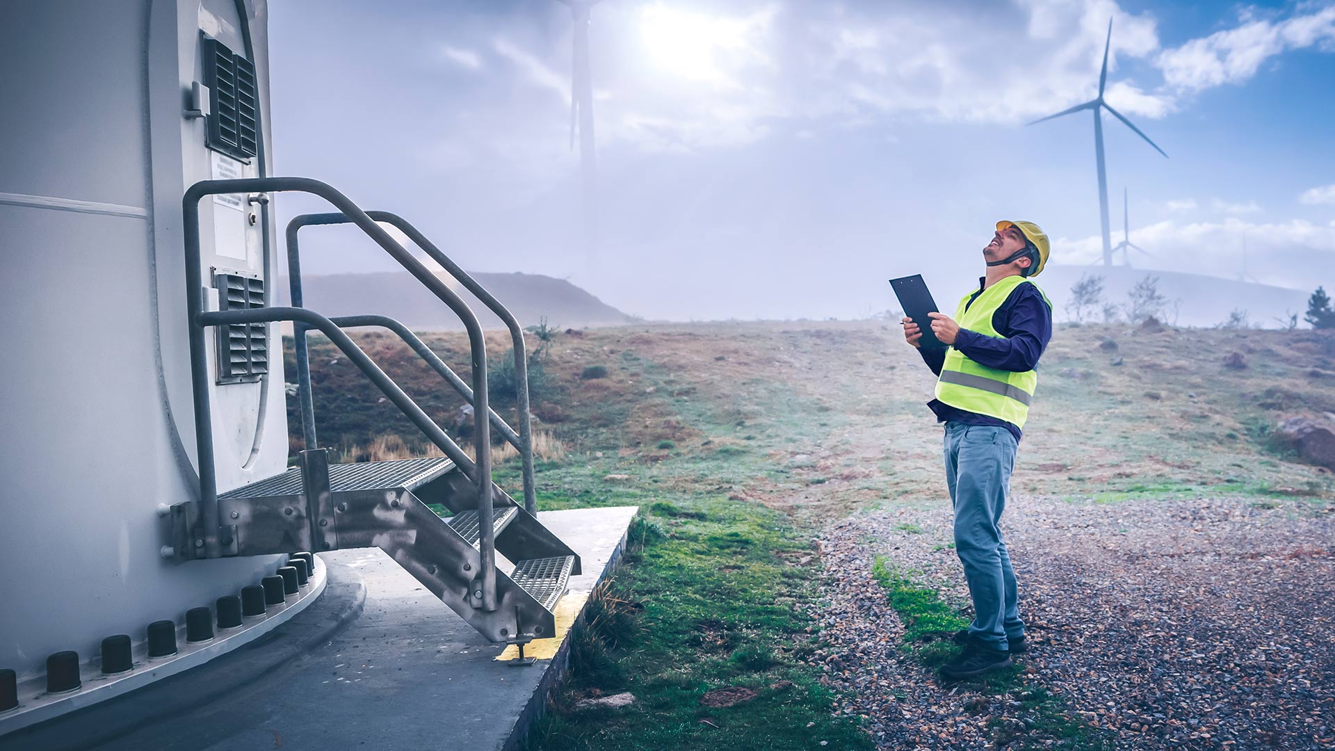 Ein Arbeiter steht mit einer Checkliste vor einem Windkraftrad