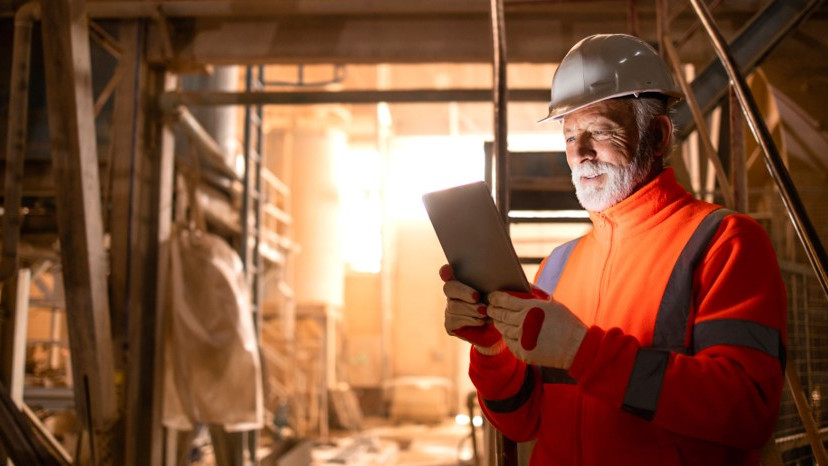 Image: Man in protective clothing on a construction site holding a tablet in his hand