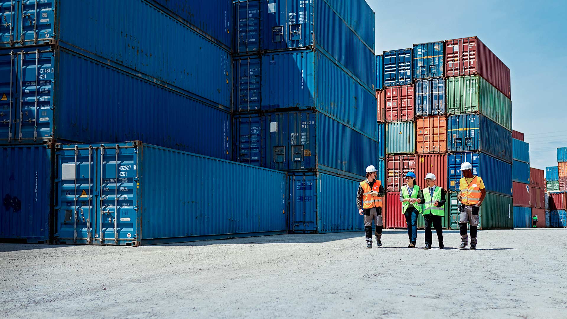 Mitarbeiter gehen über einen Containerstellplatz im Hafen