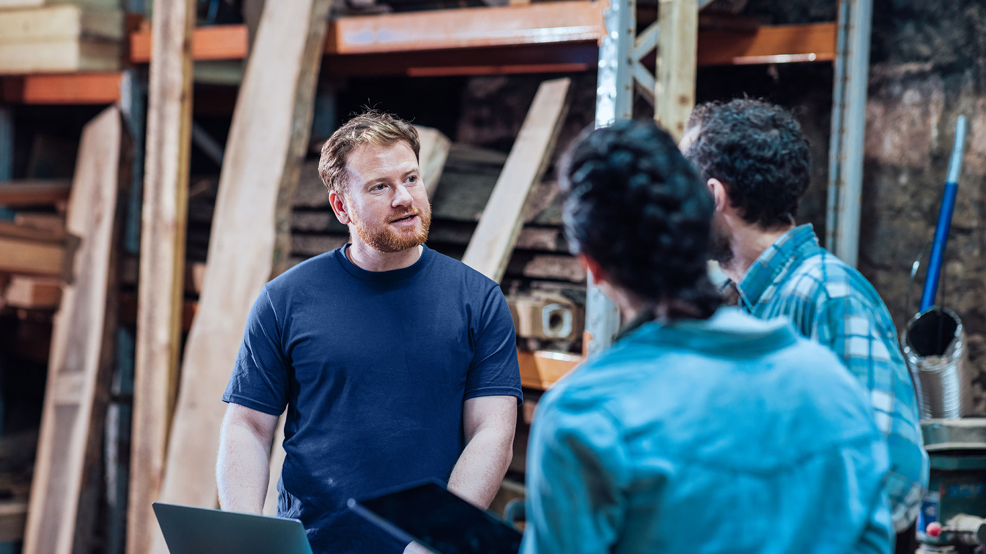 Three employees are talking in a warehouse with wooden parts