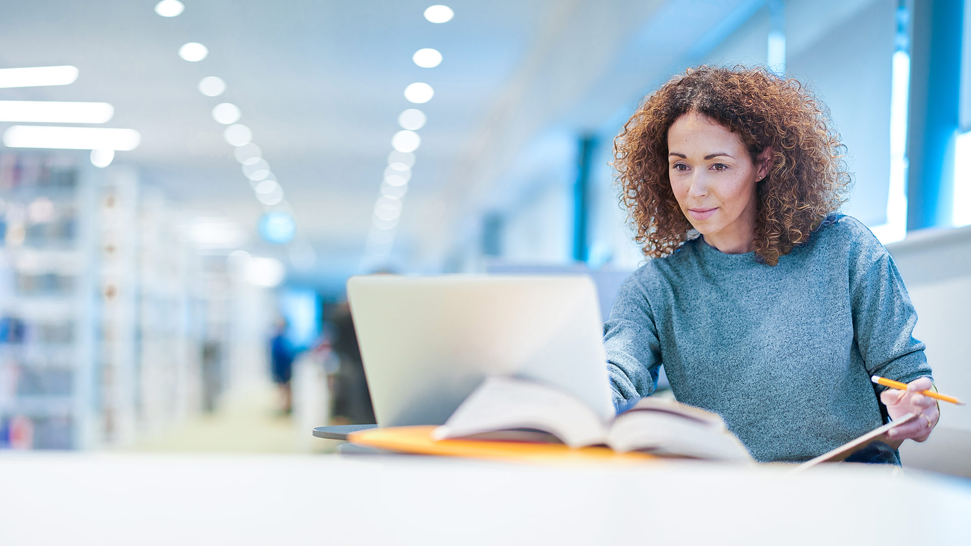 A woman looks at a laptop while holding a book