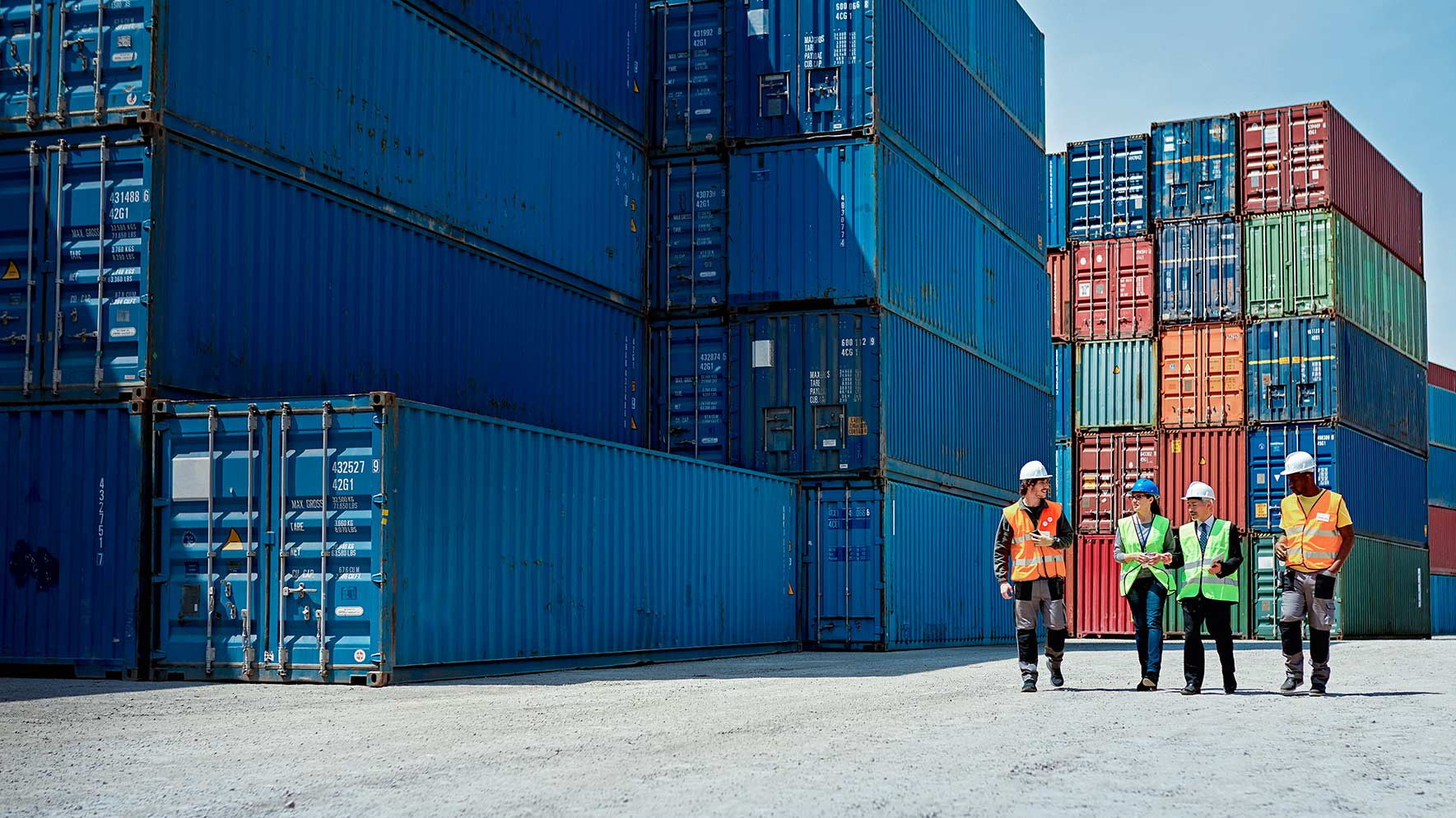 Absicherung entlang der gesamten Wertschöpfungskette Mitarbeiter gehen zwischen Containern im Hafen