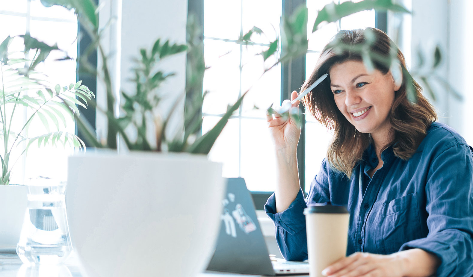 Eine Frau sitzt lächeln mit einem Kaffee vorm Laptop