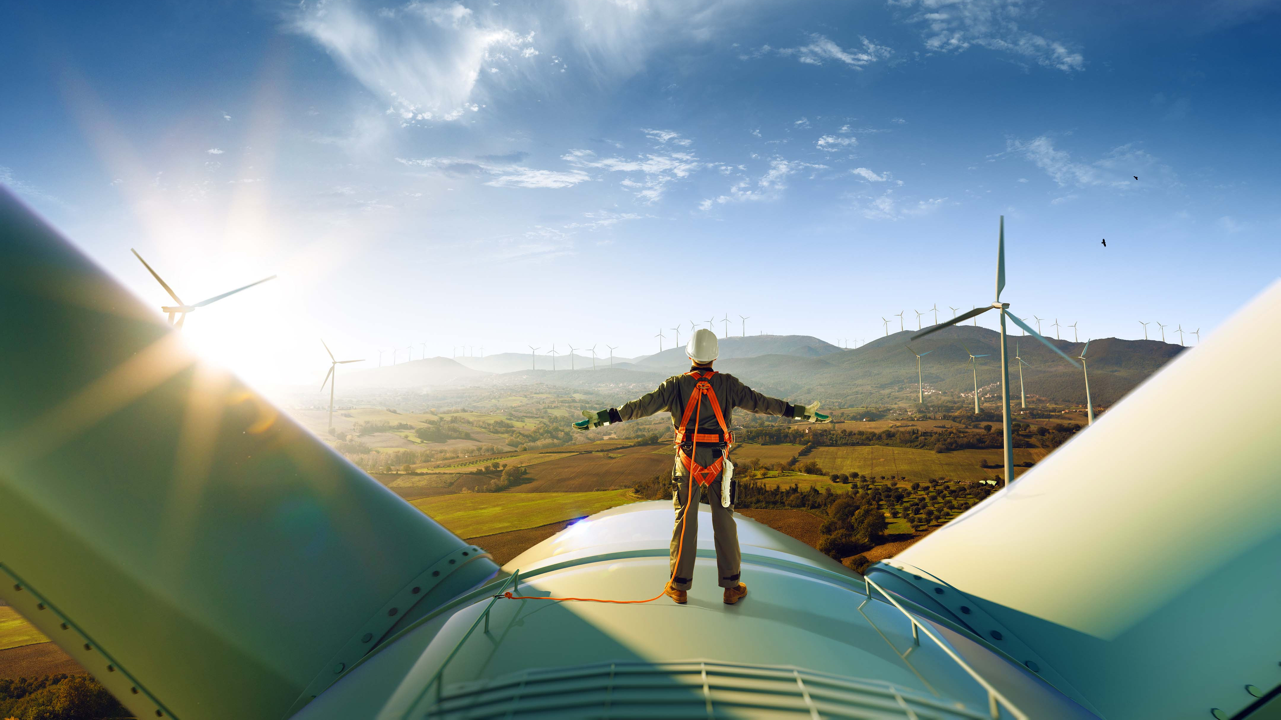 A worker stands in front of a wind turbine with a checklist