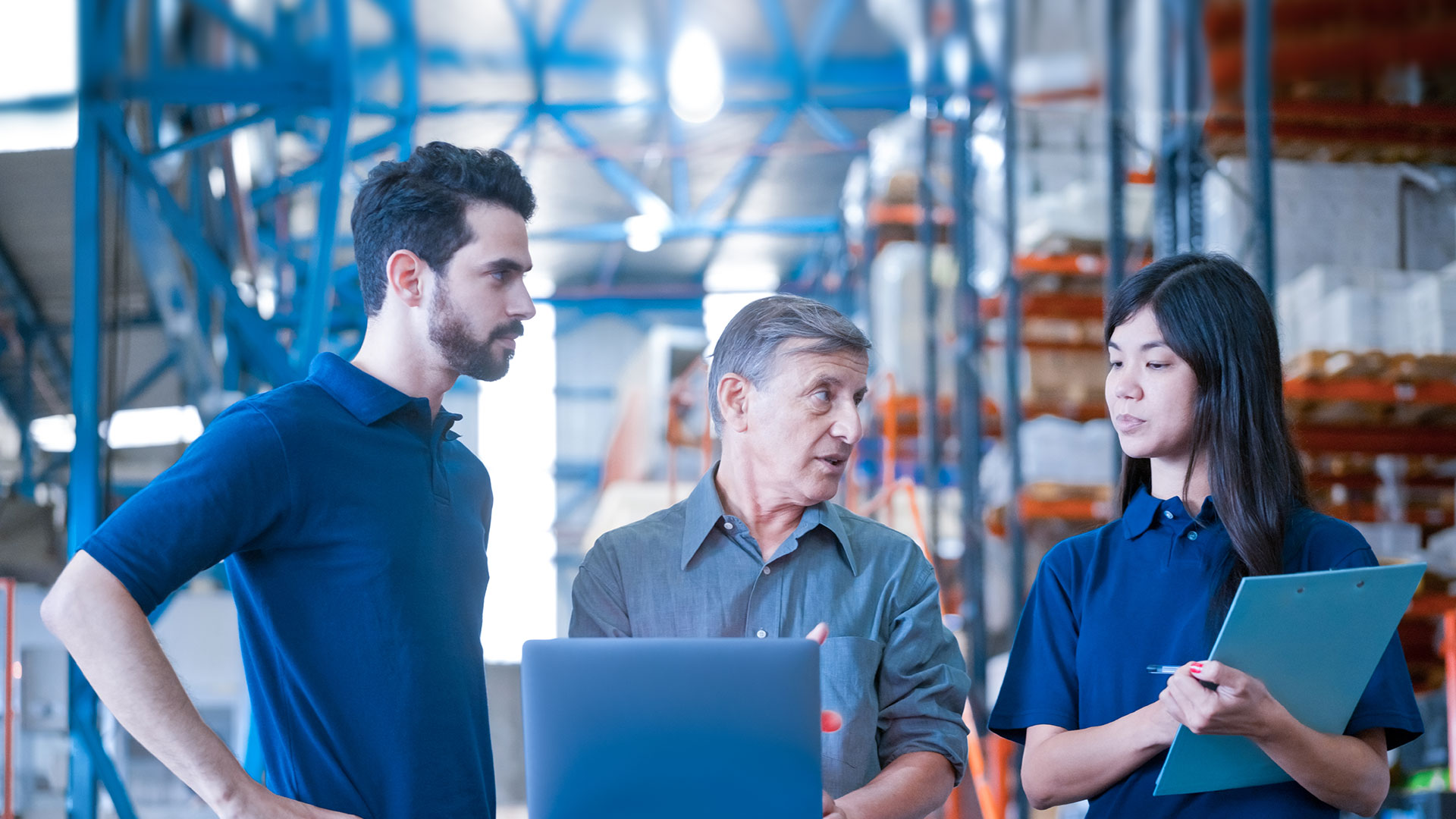 Three employees are discussing in front of a laptop in a warehouse