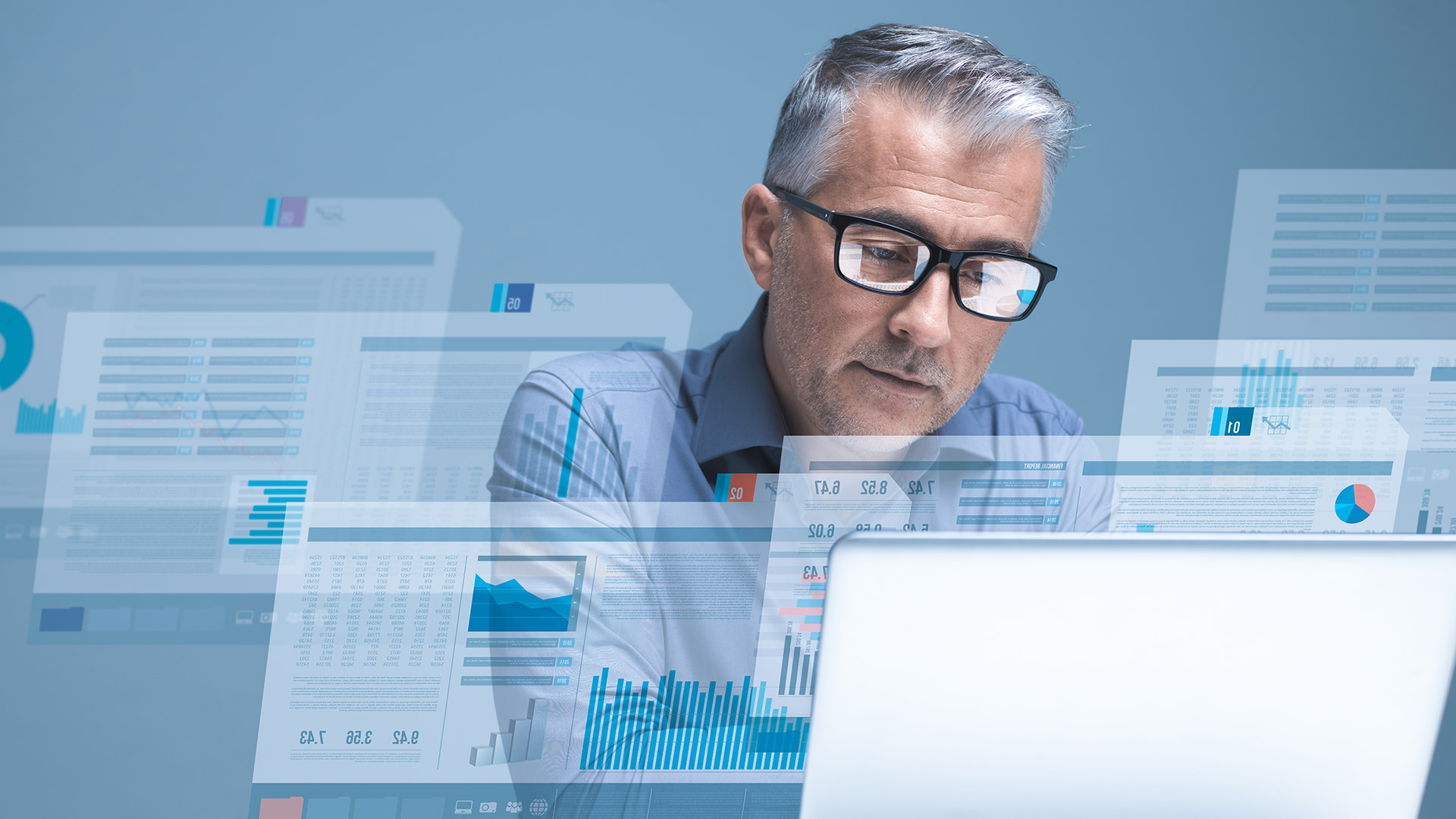 A man sits in front of various digital tables, graphics and texts