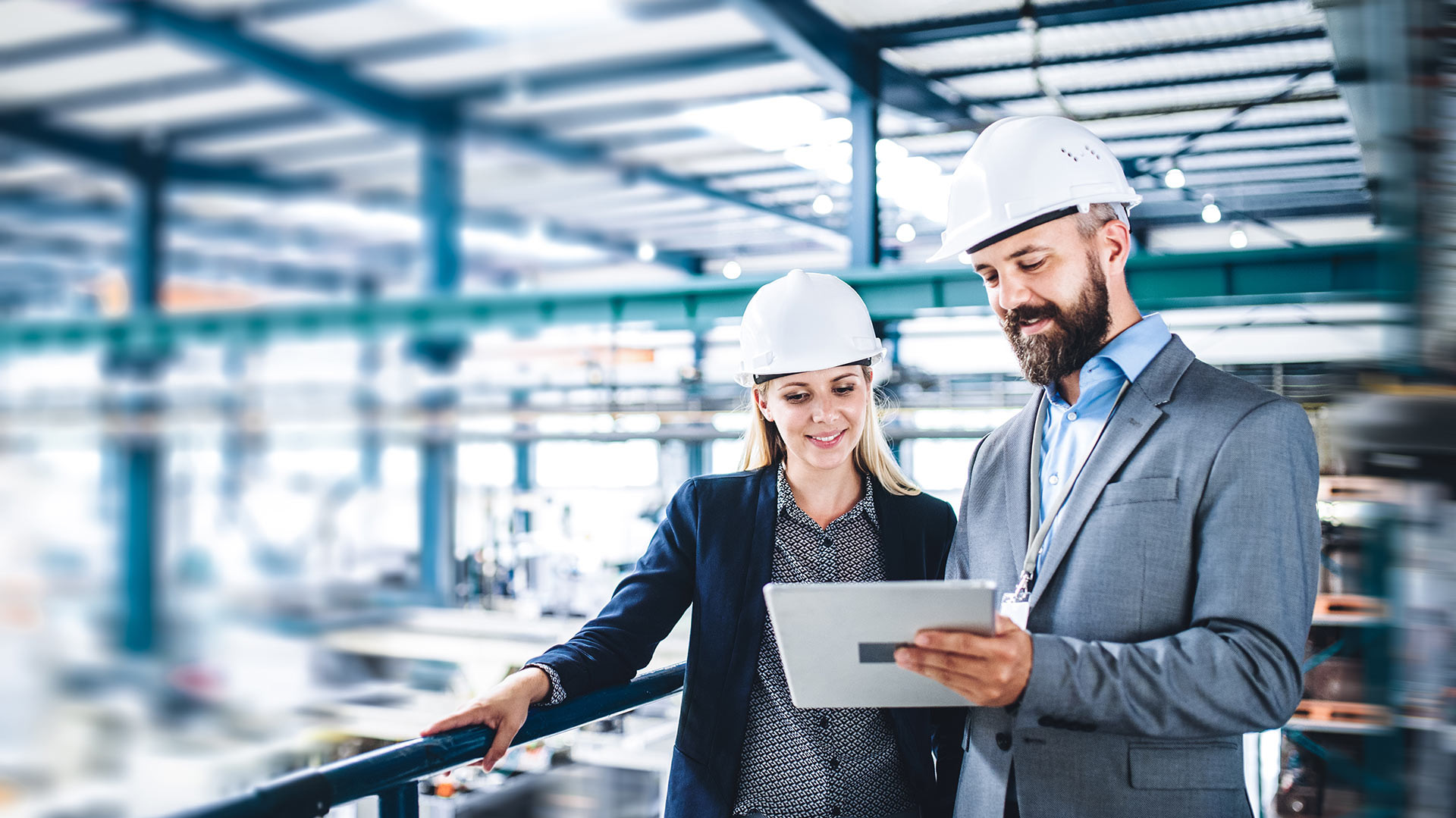 Image: 2 people in business clothes with hard hats standing on a gallery in a hall